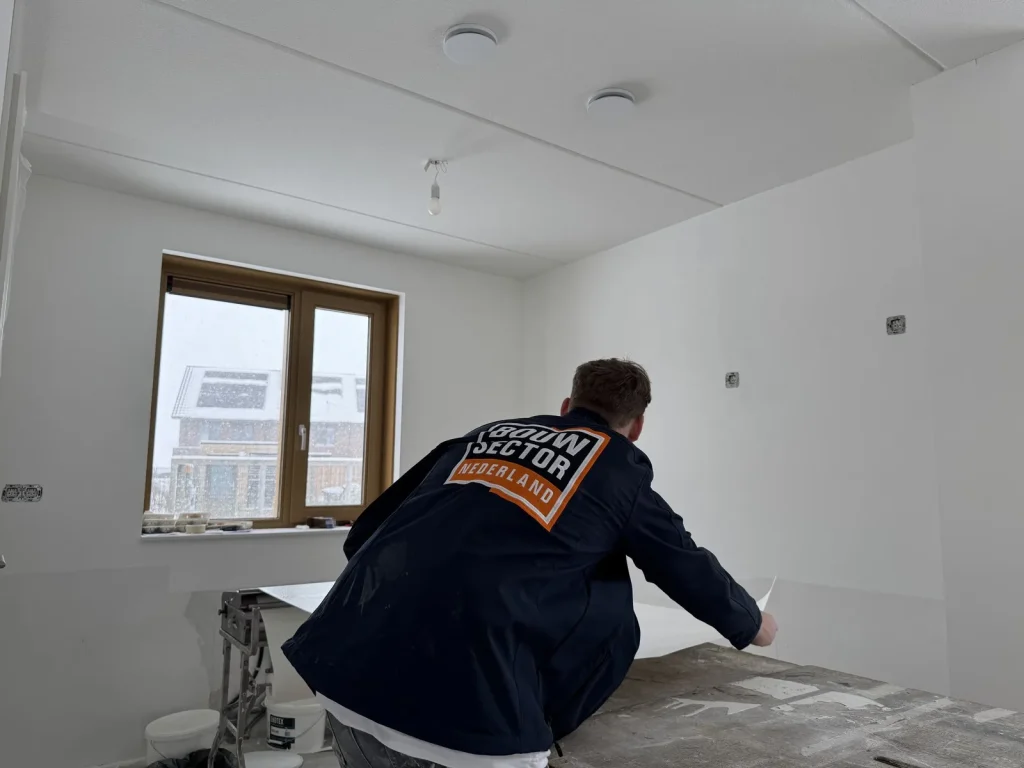 Behanger van Bouwsector Nederland trekt een ingelijmde baan vlies van de plaktafel in een nieuw huis