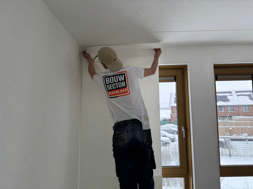Behanger drukt een baan renovlies tegen de wand onder een wit plafond