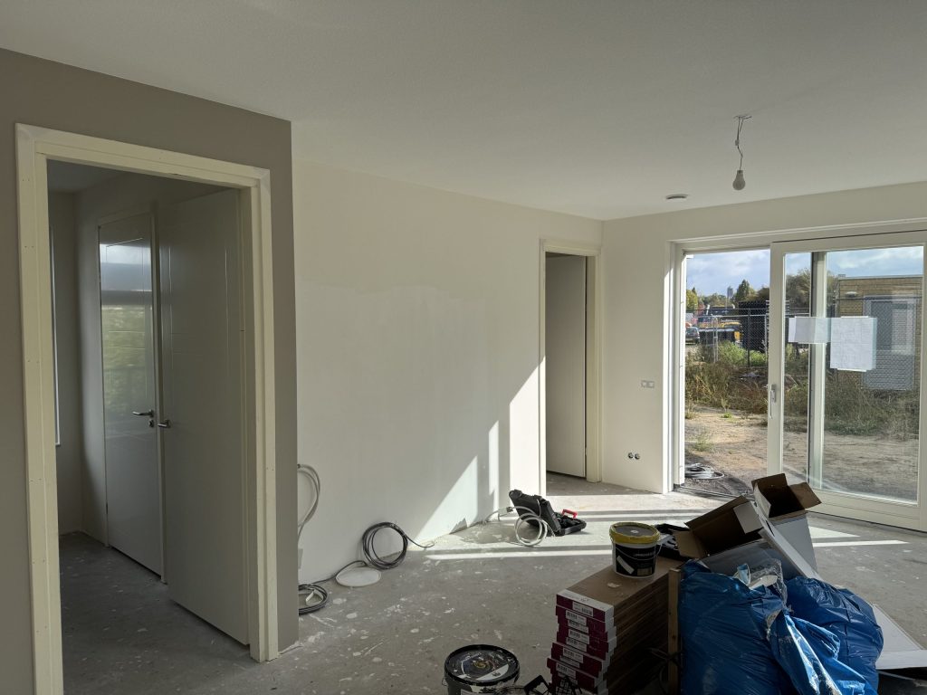 Nieuwbouwwoonkamer tijdens de afwerking, met verfemmers en dozen op de betonvloer