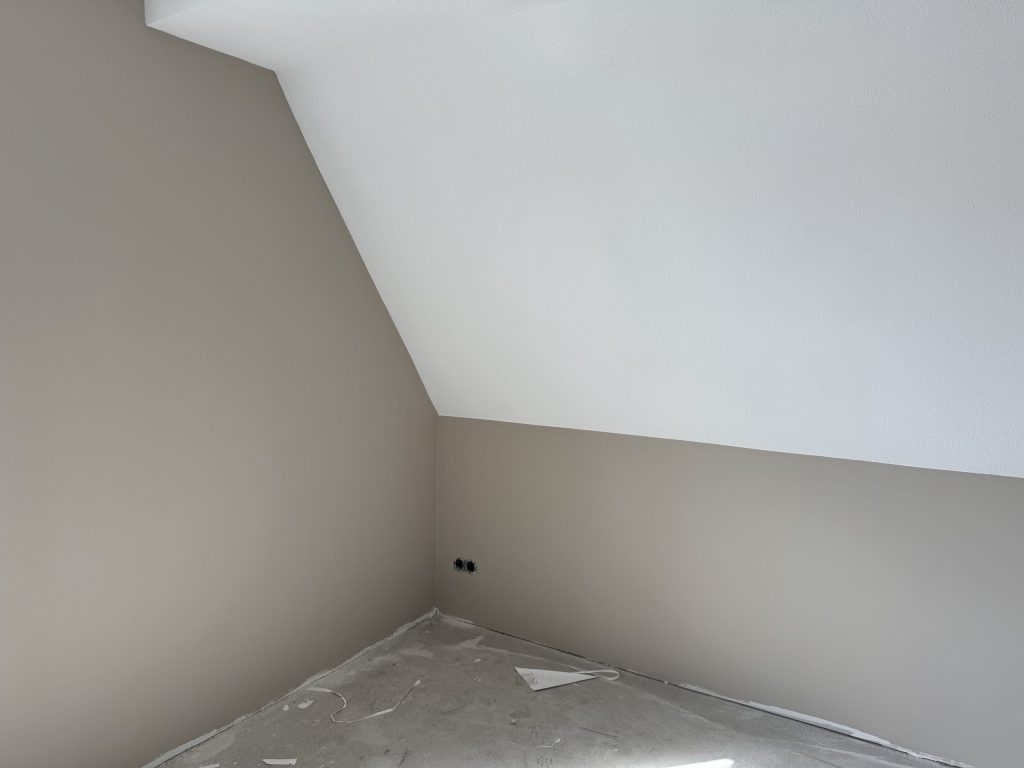 Zolderkamer van een nieuwbouwwoning met schuine wand, afgewerkte muren en nog een kale vloer