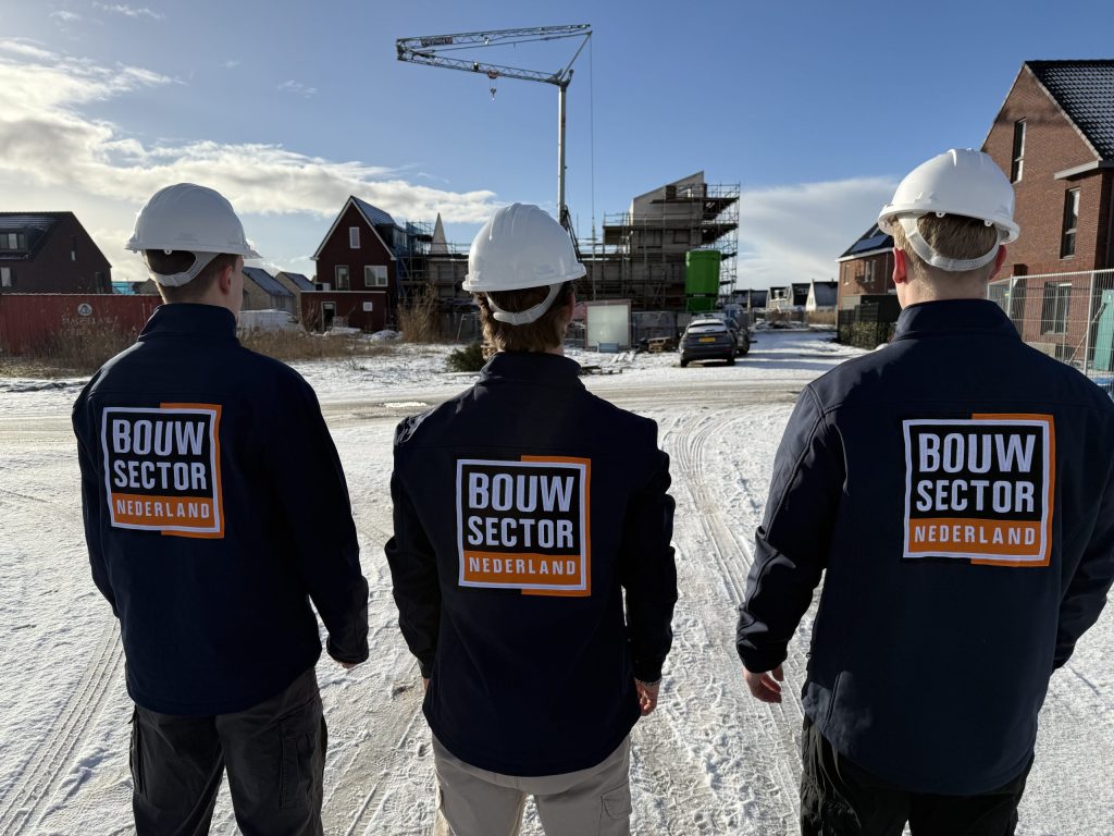 Drie vakmensen van Bouwsector Nederland met witte helm voor rijen nieuwbouwwoningen in aanbouw